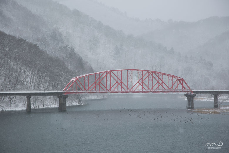 雪の降る錦秋湖と赤い鉄橋
